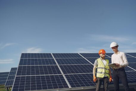 Deux professionnels équipés de casques contrôlent une installation de panneaux solaires sur un site extérieur.